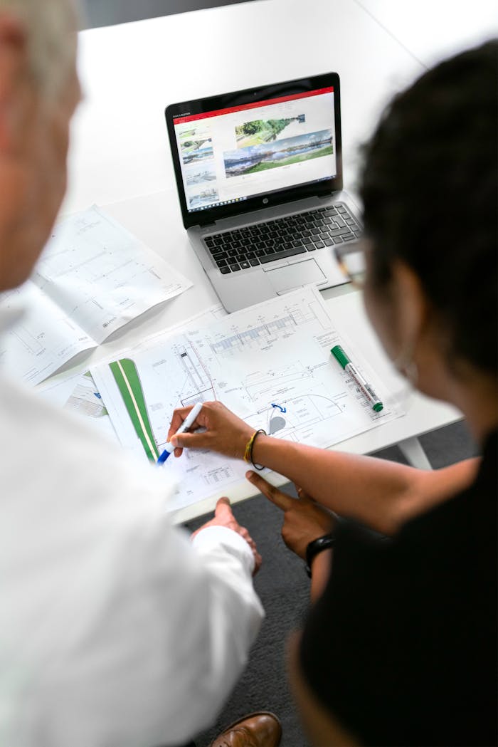 about-us Engineers collaborate on designs with blueprints and laptops in a modern office setting.
